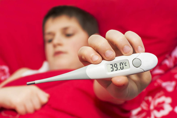 Un niño enfermo acostado en la cama muestra un termómetro
 - Foto, Imagen