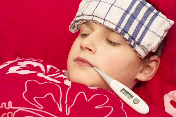 A sick boy lying in bed with a thermometer in his mouth - Photo, Image