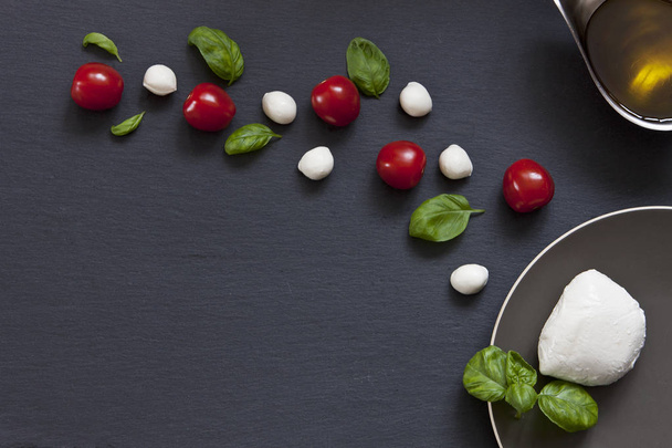 close-up of red cherry tomatoes with white mozzarella cheese and green leaves of basil on black background - Photo, image