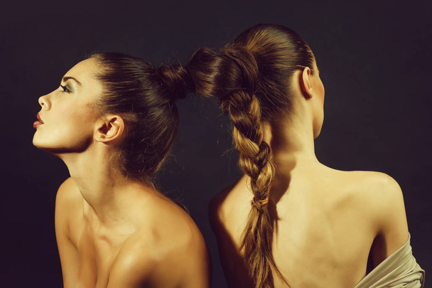 naked sexy women or pretty girls, lesbian models, with braided or tied, beautiful, healthy, brunette, long hair into braid or plait on dark background. Friendship and love - Foto, Imagen