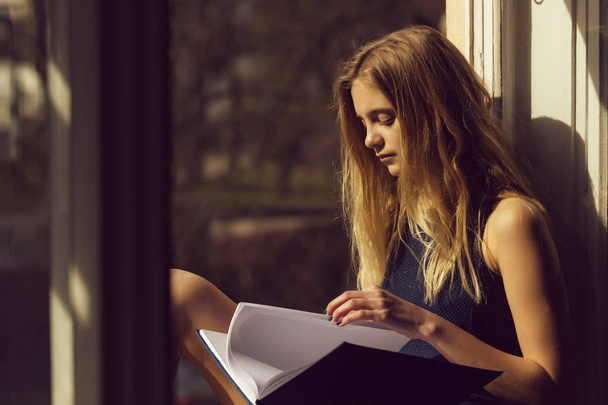 Pretty girl reading book at open window - Valokuva, kuva