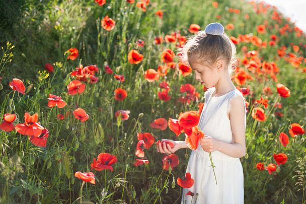 beautiful little girl collecting flowers on a slope with flowering poppies in spring - Foto, Imagem
