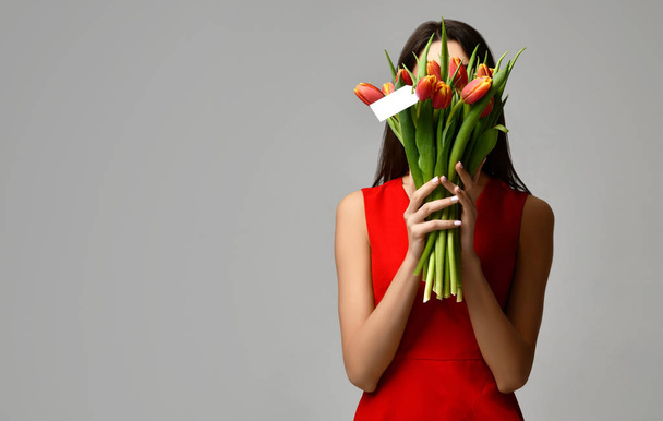 Hermosa mujer con ramo de flores de tulipán en vestido rojo y pequeña pegatina en tulipanes con espacio libre de texto vacío
 - Foto, imagen