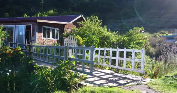 English garden with white fence, bridge, tropical vegetation and wooden hostel in mountain village  - Footage, Video