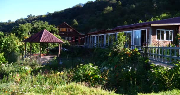 Jardín inglés con valla blanca, puente, vegetación tropical y albergue de madera en pueblo de montaña
  - Imágenes, Vídeo