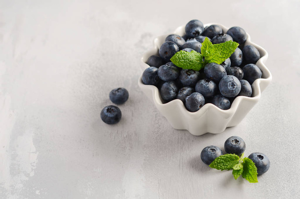 Ripe sweet blueberries in white bowl on a gray concrete background, selective focus, copy space. - Fotó, kép