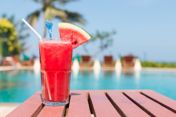 Healthy concept, Water melon smoothie on a wood table with swimming pool and blue sky background. - Foto, Imagen