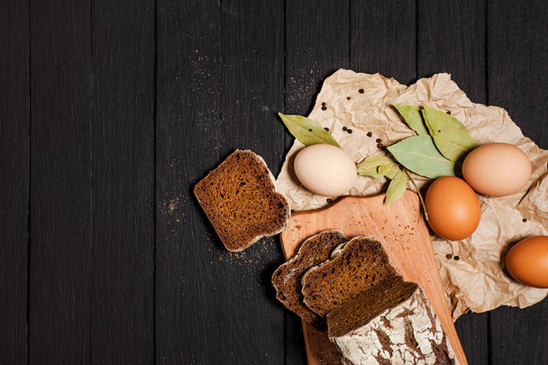 Brot, Eier, Gewürze und verschiedene Gewürze liegen auf einem dunklen Hintergrund. Blick von oben. - Foto, Bild