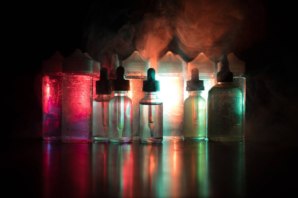 Vape concept. Smoke clouds and vape liquid bottles on dark background. Light effects - Photo, Image