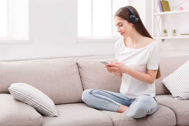 Young woman with cell phone and headphones on beige couch - Фото, изображение