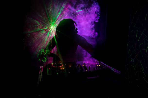 DJ dreht, mischt und kratzt in einem Nachtclub, Hände von DJ zwicken verschiedene Trackregler auf dem DJ-Deck, Blitzlicht und Nebel, oder DJ mischt den Track im Nachtclub auf der Party - Foto, Bild