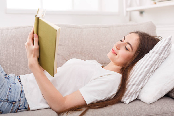 Happy young woman reading book on sofa - Fotografie, Obrázek