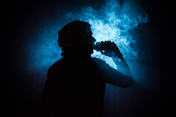 Vaping mężczyzna trzymając mod. Chmurę pary wodnej. Czarne tło. Vaping elektroniczny papieros z dużo dymu. Koncepcja Vape - Zdjęcie, obraz