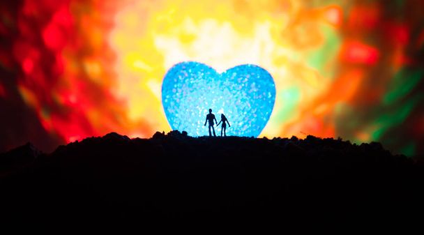Sziluettjét a boldog pár mögöttem nagy alakú szív szimbólum a hegyre éjjel. Nagy szíve, mint a ködös égen ragyogó Hold. Valentin napi dekor fénykép - Fotó, kép