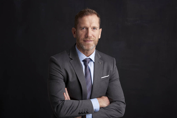 Portrait of middle aged wrinkled businessman with arms crossed wearing suit while posing at dark background. - Valokuva, kuva