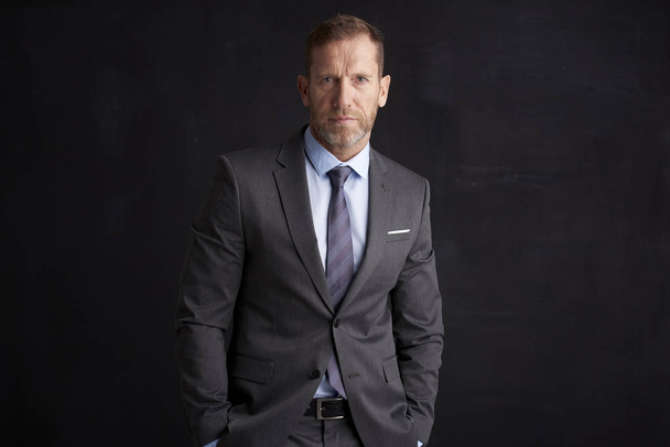 Portrait of an executive financial businessman wearing suit while standing at dark background.  - Fotó, kép