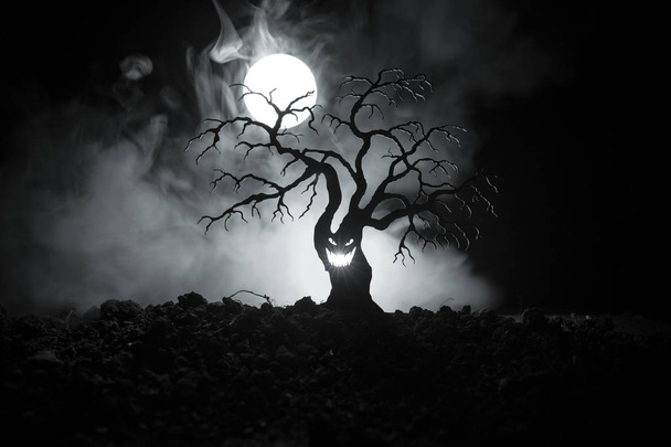 Силуэт пугающего Хэллоуинского дерева с ужасающим лицом на темном туманном фоне с луной на задней стороне. Страшное дерево ужасов с зомби и демоническими лицами
. - Фото, изображение