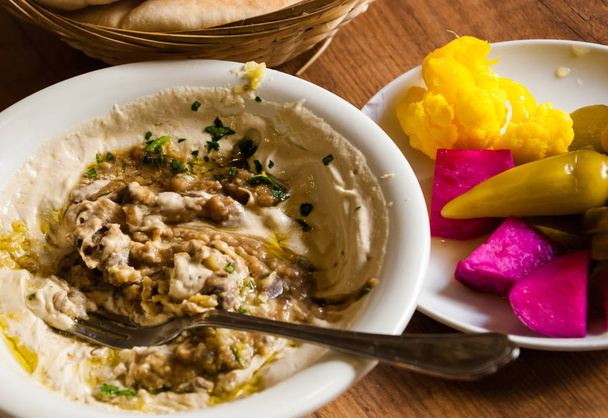 Fresh delicious hummus with broad beans dish, pita bread and colorful spicy pickles (hot chili pepper, cauliflower, cucumbers,  turnip) served in the traditional restaurant in Jaffa (Israel). - Fotó, kép