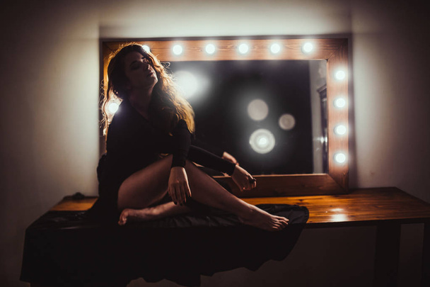 portrait of young beautiful red hair woman in black dress near mirror with light bulbs - Photo, image