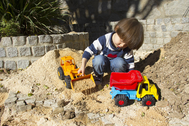 little three year old boy playing in the sand with a digger and dump truck. - Foto, immagini