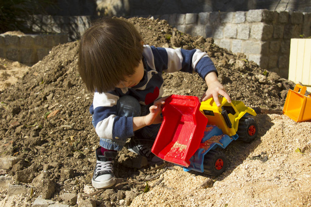 bir kazıcı ve damperli kamyon kum oynarken küçük üç yıl yaşlı erkek çocuk. - Fotoğraf, Görsel