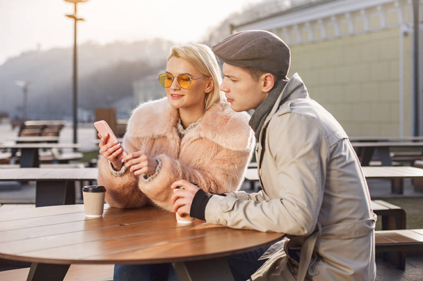 Positive couple is enjoying espresso and watching picture on mobile - Фото, изображение