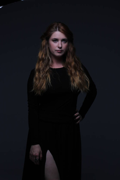 young beautiful red hair woman in black dress on dark background - 写真・画像