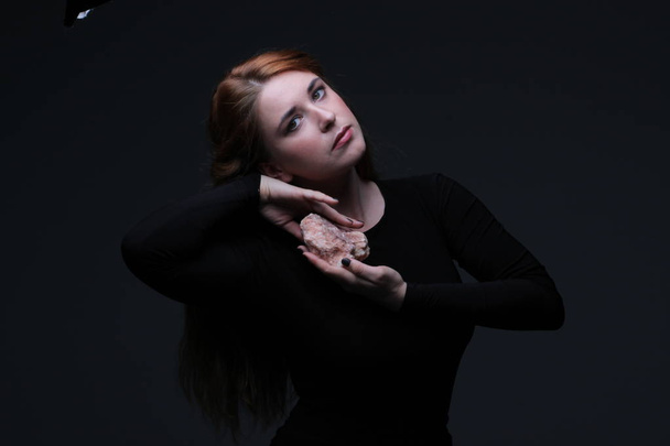 young beautiful red hair woman in black dress holding sea stone on dark background - Foto, immagini
