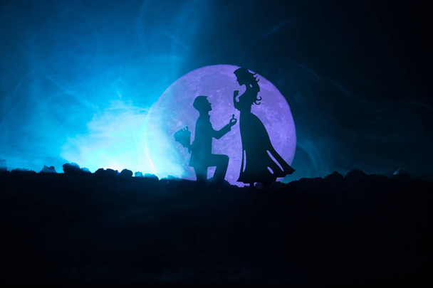 Καταπληκτική σκηνή αγάπης. Σιλουέτες του ανθρώπου κάνει πρόταση σε γυναίκα ή σιλουέτες των δυο ενάντια σε μεγάλο φεγγάρι στο παρασκήνιο - Φωτογραφία, εικόνα