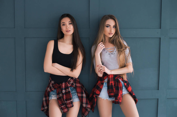 ewig jung! ein Outdoor-Foto von zwei jungen sexy Models, die isoliert vor dem grauen Wandhintergrund in rotem kariertem Hemd und Shorts vor der Kamera posieren. - Foto, Bild