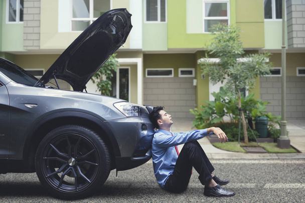 Frustrated businessman feeling hopeless leaning on his breakdown car - Foto, Imagem