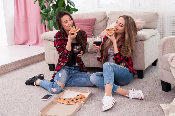Через толстые и тонкие остаться друзьями навсегда! Расслабленные привлекательные молодые улыбающиеся дамы пьют вино и едят пиццу дома
. - Фото, изображение