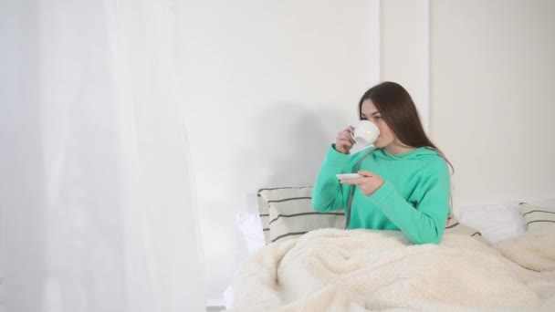 Μια νεαρή γυναίκα ξύπνησε πρόσφατα και πίνει ζεστό καφέ από ένα φλιτζάνι - Πλάνα, βίντεο