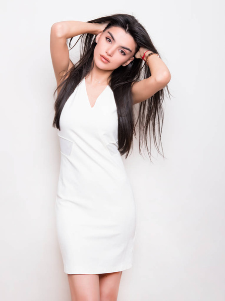 beautiful young woman with long black hair wearing dress and posing on white background - Фото, зображення