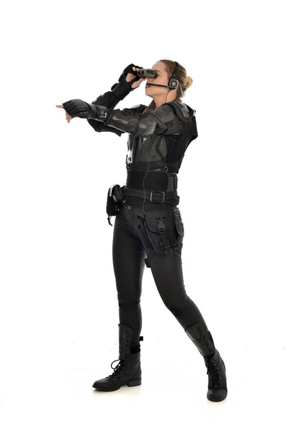 портрет женщины-солдата в черных тактических доспехах с биноклем на белом фоне студии
. - Фото, изображение