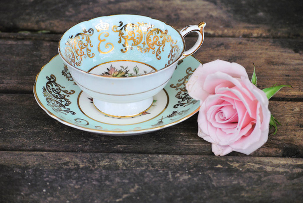 A decorative still life of porcelain teacup and saucer with roses, against a rustic background of weathered wood. The cup is a Paragon China collectable titled, "To Her Majesty The Queen". A beautiful image for love, wedding, and garden designs.  - Photo, Image