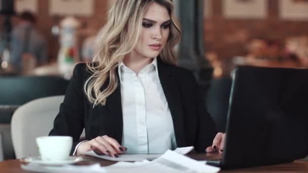 una giovane donna in abiti da lavoro che lavora su un computer portatile seduto a un tavolo in un caffè. donna d'affari che lavora in un ambiente informale
 - Filmati, video