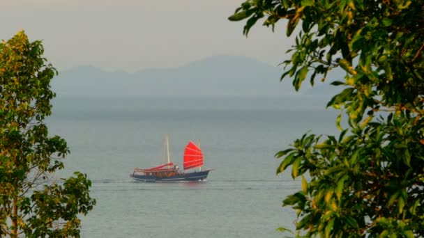 A traditional chinese ship with red sails floats along the sea at sunset - Filmagem, Vídeo