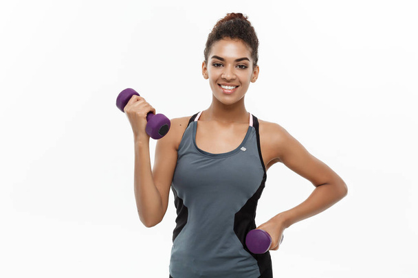 Healthy and Fitness concept - Beautiful American African lady in fitness clothes workout with dumbbell. Isolated on white background. - Photo, Image
