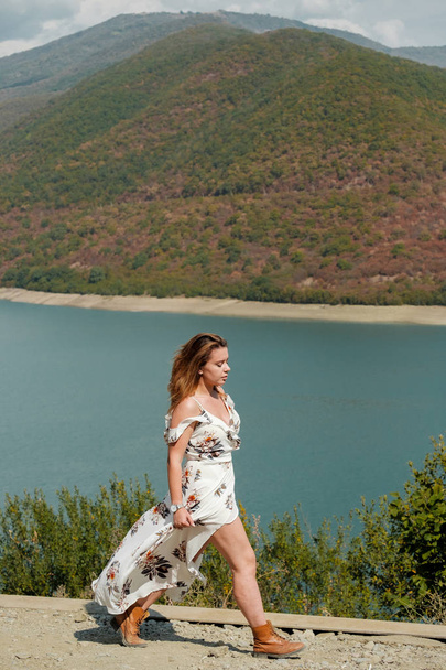 Beautiful girl in a long dress on a background of a lake and mountains - 写真・画像