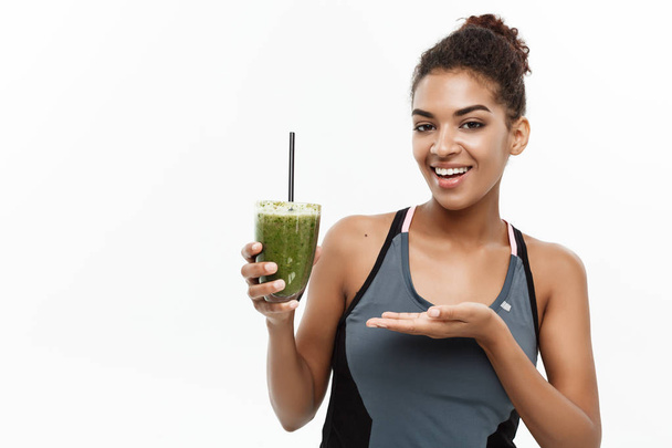 Healthy and Fitness concept - Beautiful American African lady in fitness clothing drinking healthy vegetable drink. Isolated on white background. - Φωτογραφία, εικόνα