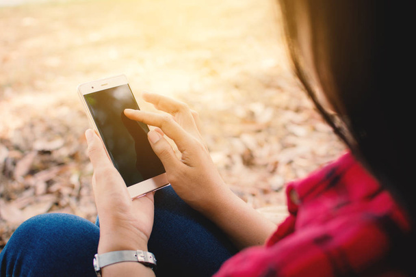 Nautitaan hetki nainen käyttää älypuhelinta istuu suuren puun alla puistossa, rentoutua aikaa loma käsite, väri vuosikerta
 - Valokuva, kuva