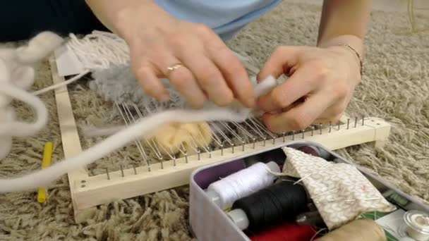 Una mujer teje en un telar un hermoso bordado hecho de hilo, en un estudio en casa
, - Metraje, vídeo