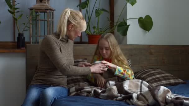 Caring mother giving her ill daughter hot tea - Кадры, видео
