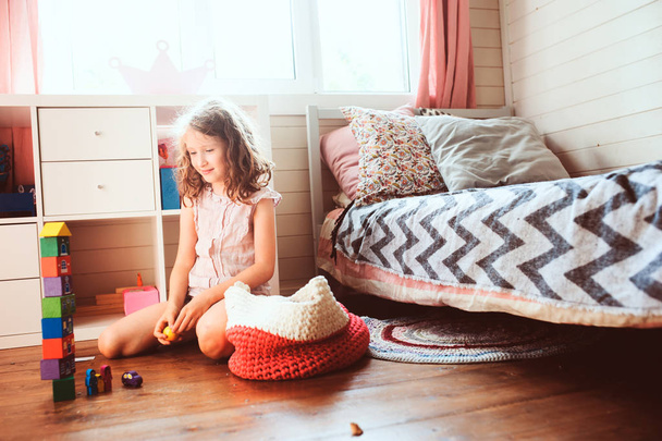 child girl cleaning her room and organize wooden toys into knitted storage bag. Housework and help concept - 写真・画像