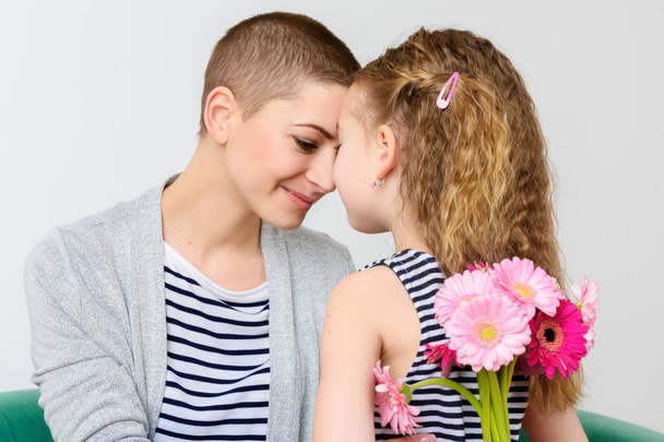 Happy Mother's Day, Women's day or Birthday background. Cute little girl giving mom, cancer survivor,  bouquet of pink gerbera daisies. Mother and daughter smiling. - Fotó, kép