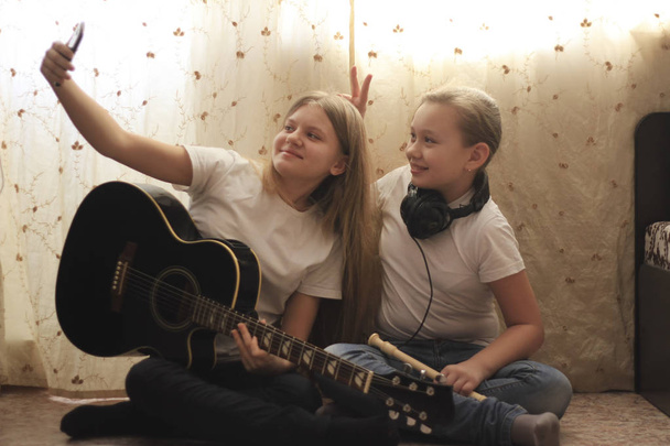 zwei weibliche Teenager machen Selfie und posieren mit Musikinstrumenten, die zu Hause auf dem Boden sitzen - Foto, Bild