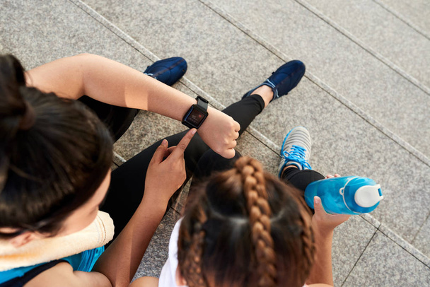 Mulheres esportivas verificando na tela do relógio inteligente para sua amiga
 - Foto, Imagem
