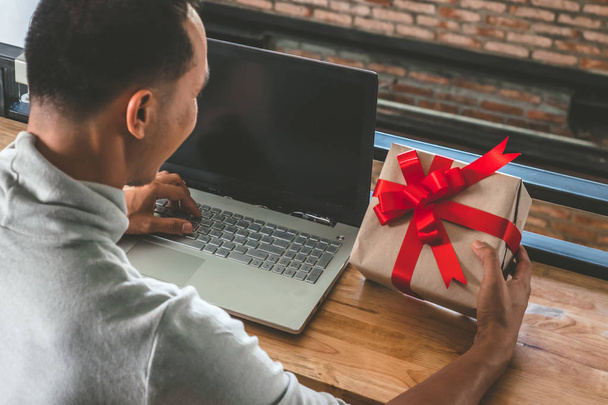 Щаслива людина тримає подарунковій коробці і використовуючи ноутбук на столі. Азіатських людині підготовка представляє для різдвяних свят. - Фото, зображення