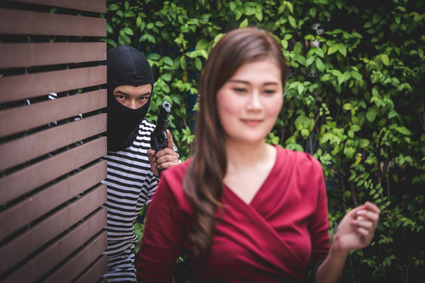 Dief houdt een pistool en Aziatische vrouw, die is wandelen alleen, te kijken en wachten op haar tas stelen. - Foto, afbeelding